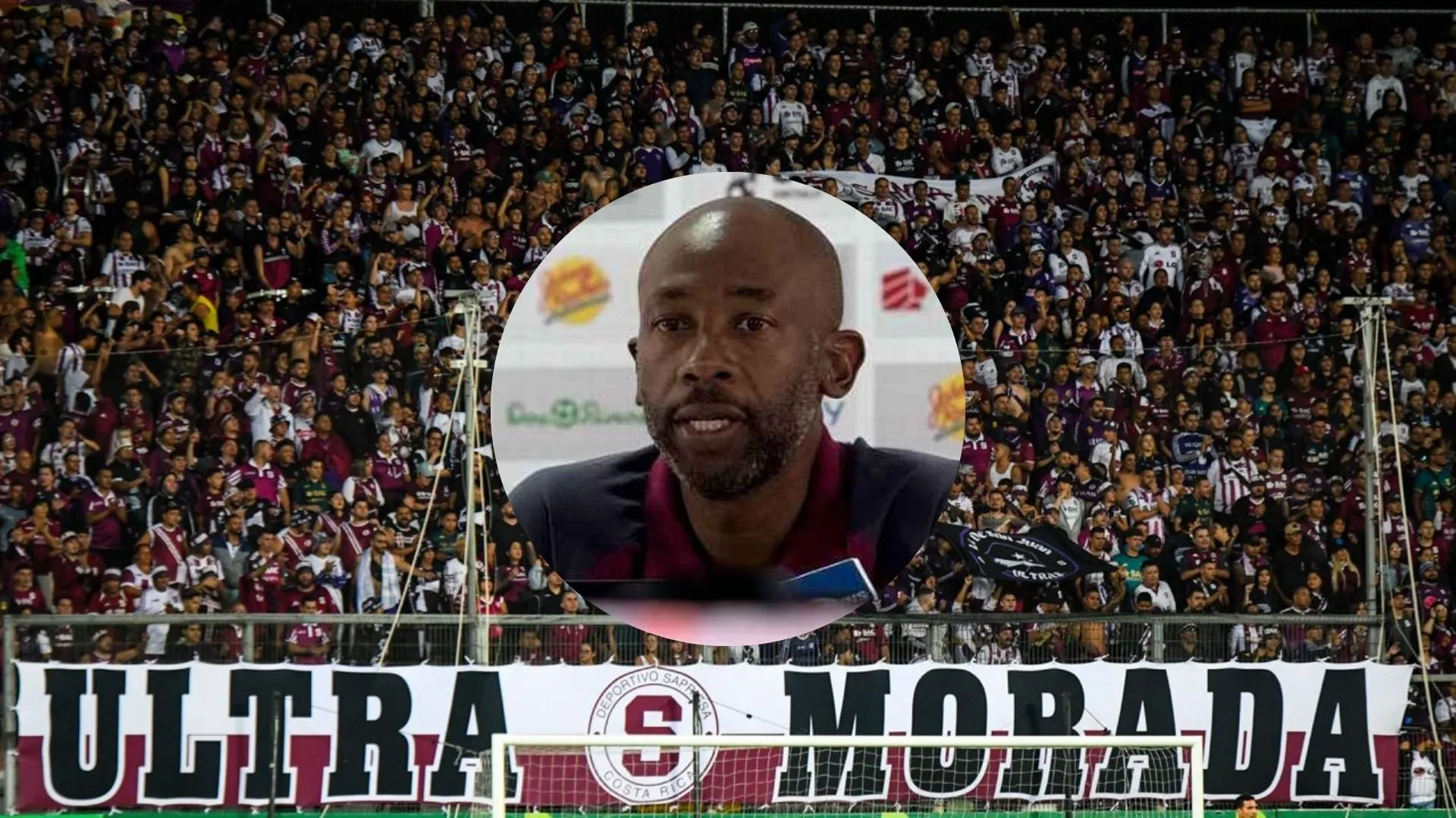 Paulo Wanchope en conferencia y la afición morada de fondo.